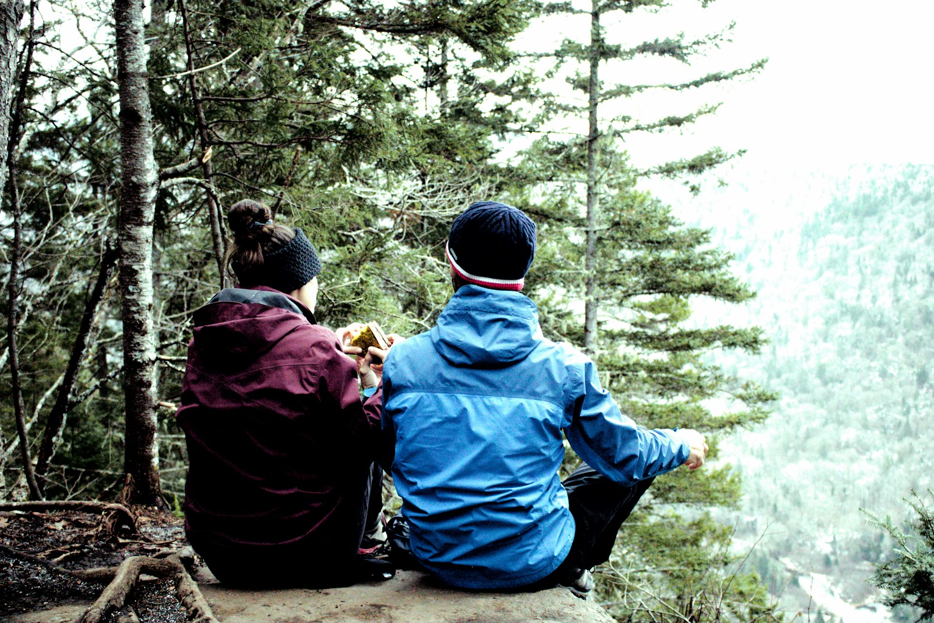 two people sitting on a rock in the woods